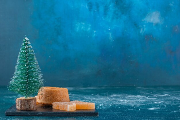 Marmelades, un petit gâteau et une figurine d'arbre sur un tableau noir sur fond bleu. Photo de haute qualité