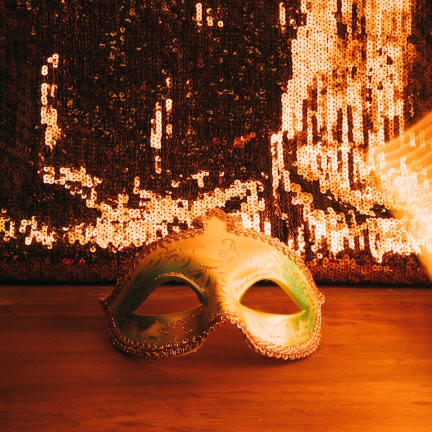 Masque de carnaval vert sur un bureau en bois avec des paillettes de paillettes d&#39;or