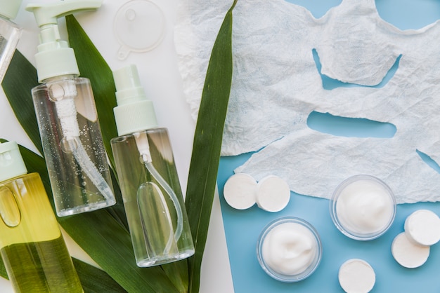 Photo gratuite masque facial en feuille de papier; vaporisateurs de crème et à base de plantes avec des feuilles sur fond bleu