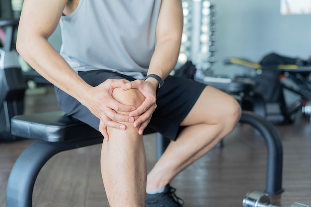 Massage de la main de l'homme sur le genou après l'entraînement et ressentir la douleur de courir au club de gym