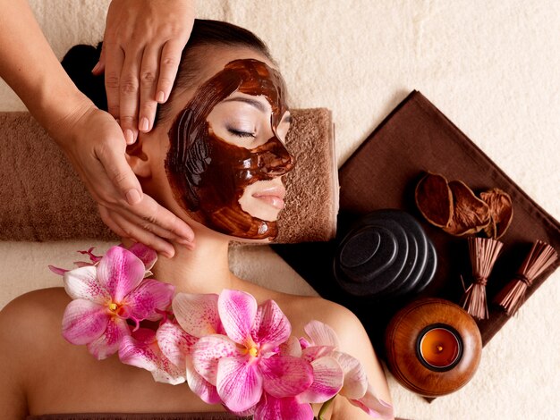 Massage spa pour jeune femme avec masque facial sur le visage - à l'intérieur