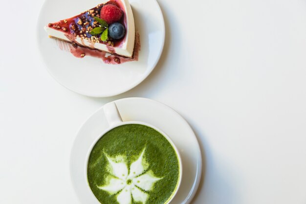 Matcha thé vert japonais dans la tasse blanche et gâteau aux baies au fromage sur plaque sur fond blanc