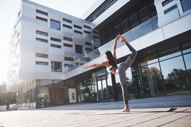 Matin d'été ensoleillé. Jeune femme athlétique faisant le poirier sur la rue du parc de la ville parmi les bâtiments urbains modernes. Faites de l'exercice en plein air mode de vie sain