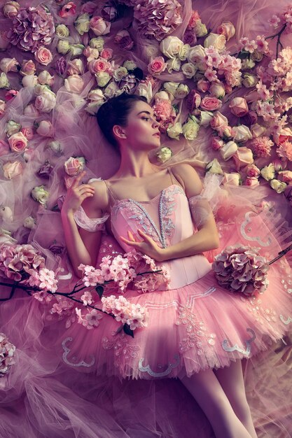 Âme épanouie. Vue de dessus de la belle jeune femme en tutu de ballet rose entouré de fleurs. Ambiance printanière et tendresse dans la lumière corail. Photographie d'art. Concept de printemps, de floraison et d'éveil de la nature.