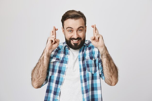 Un mec barbu excité et plein d'espoir croise les doigts, priant