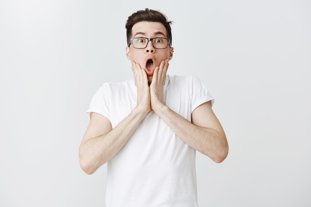 Un mec choqué et impressionné à lunettes, laisse tomber la mâchoire et regarde étonné