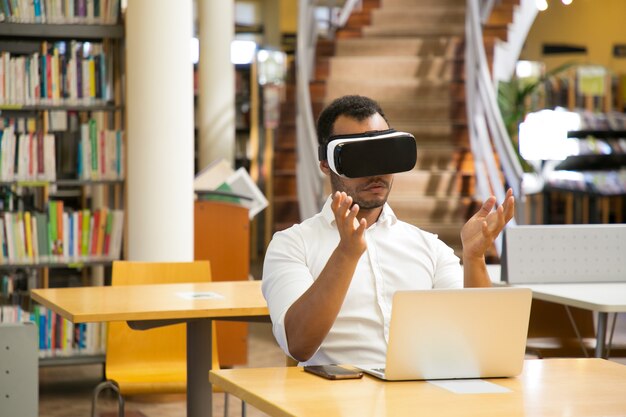 Mec concentré avec casque VR assis dans la bibliothèque