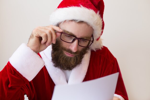 Mec concentré portant le costume de père Noël et un document de lecture