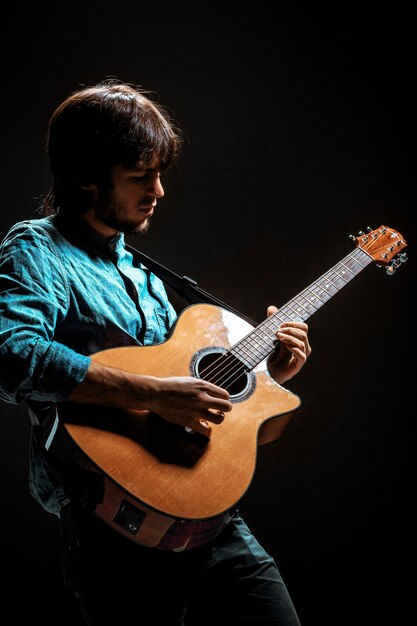 Mec cool avec chapeau debout avec guitare sur fond sombre de studio