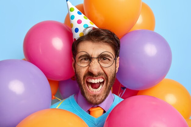 Mec ennuyé entouré de ballons de fête posant