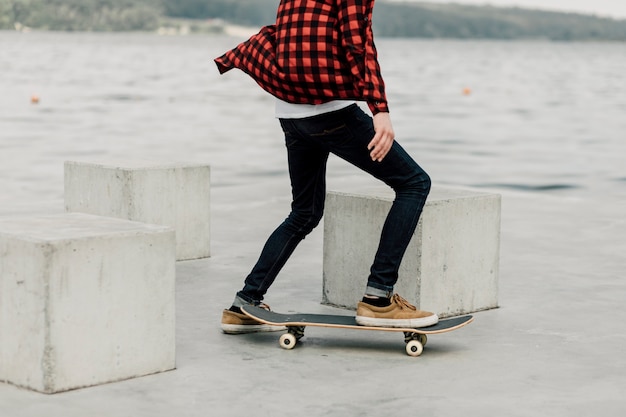 Mec en flanelle faisant de la planche à roulettes au bord du lac