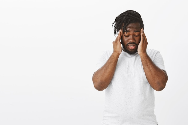 Mec flou avec des tresses posant contre le mur blanc