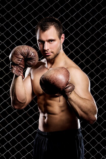 Mec avec des gants de boxe montrant les muscles sur la clôture