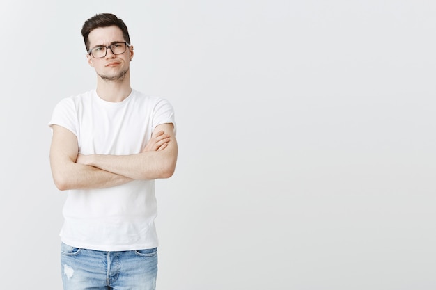 Mec hésitant à lunettes, poitrine croisée et sourire narquois, regardant avec incrédulité