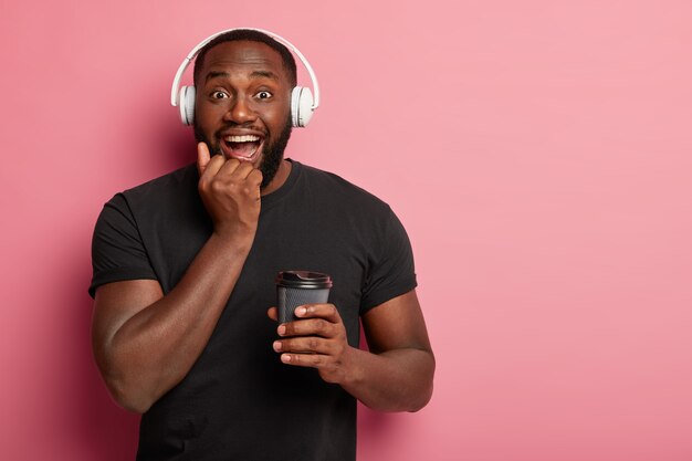 Un mec heureux se sent détendu pendant le rituel régulier du matin, écoute de la musique de motivation dans le casque, apprécie parfaitement le café et la chanson