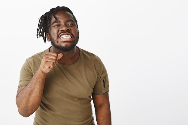 Un mec indigné dans un t-shirt marron posant contre le mur blanc