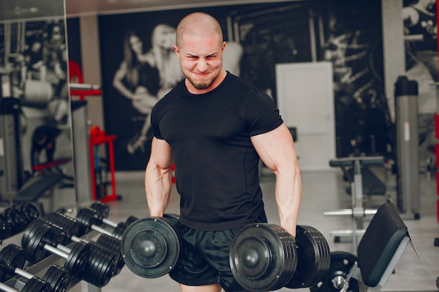 Un Mec Jeune Et Musclé Dans Un T-shirt Noir S'entraîne Dans Une Salle De Sport