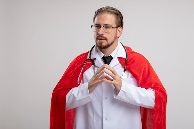 Mec jeune super-héros suspect portant une robe médicale avec stéthoscope et lunettes tenant par la main ensemble isolé sur fond blanc