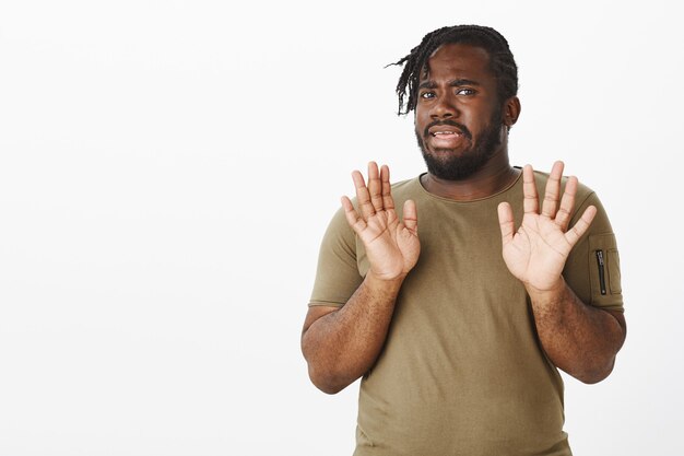 mec mécontent dans un t-shirt marron posant contre le mur blanc