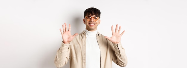 Photo gratuite mec moderne dans des verres et tenue élégante montrant le nombre de dix doigts et souriant debout sur ba blanc