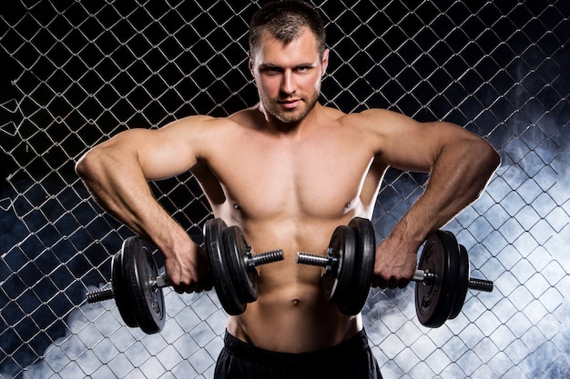 Photo gratuite mec puissant avec un haltères montrant les muscles sur la clôture