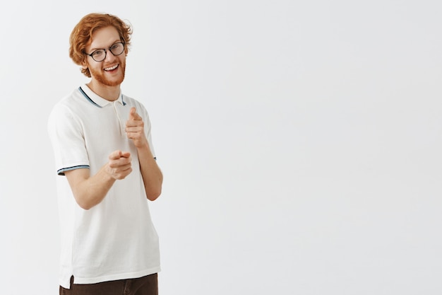 Mec rousse barbu impertinent posant contre le mur blanc avec des lunettes