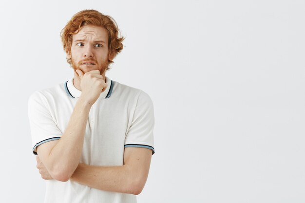 Un mec rousse barbu inquiet posant contre le mur blanc