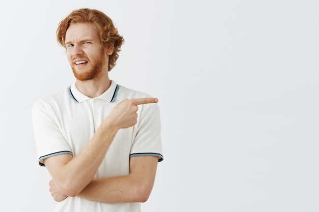 Photo gratuite mec rousse barbu mécontent posant contre le mur blanc