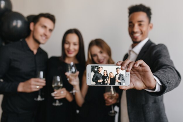 Mec souriant avec coupe de cheveux à la mode faisant selfie avec des amis pendant la fête