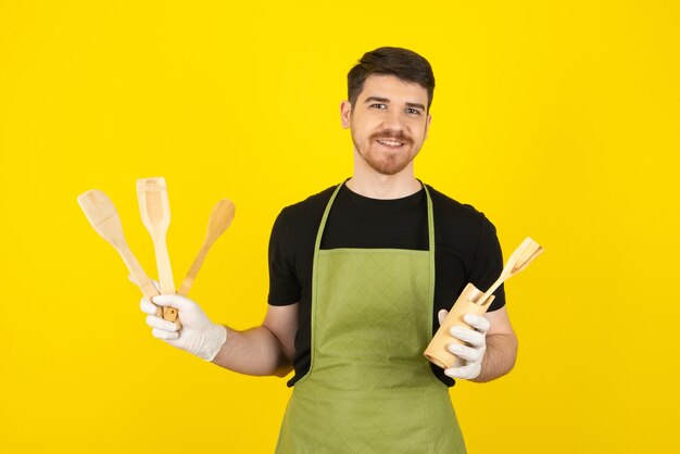 Mec souriant tenant des cuillères en bois sur un jaune.