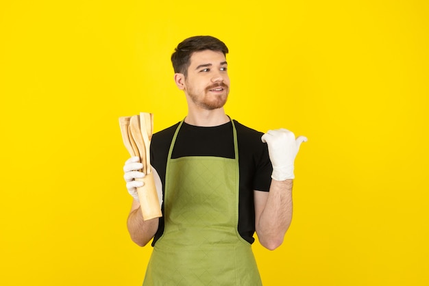 Mec souriant tenant des cuillères de cuisine en bois et regardant loin sur un jaune.