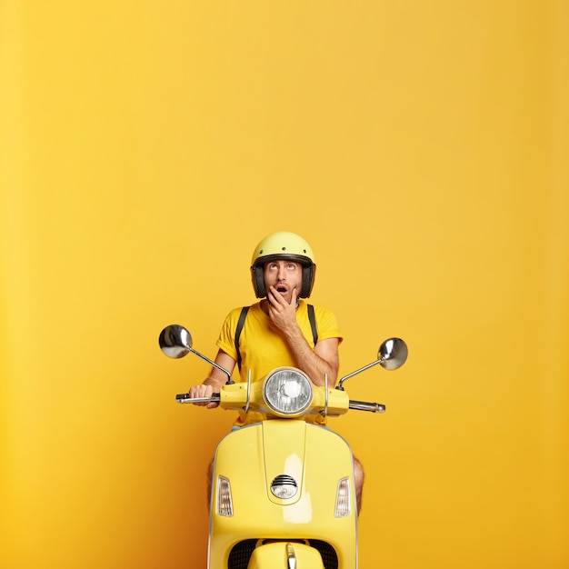 Photo gratuite mec surpris avec casque de conduite scooter jaune