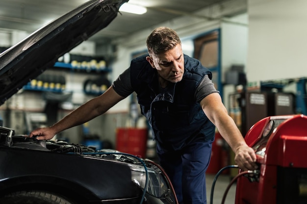 Photo gratuite mécanicien adulte moyen faisant l'entretien de l'unité de climatisation de la voiture dans un atelier de réparation automobile