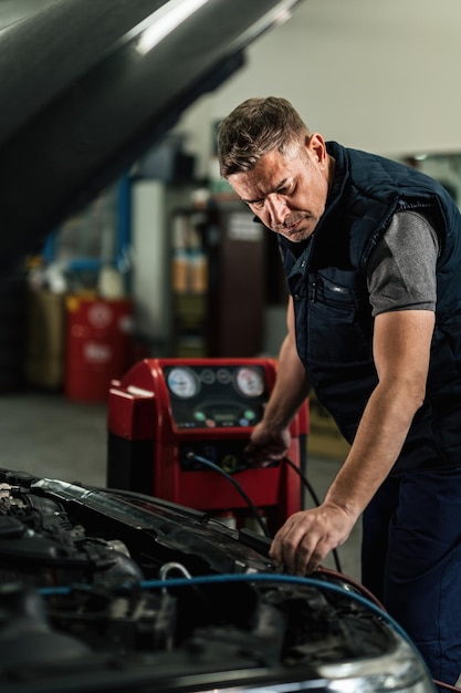 Photo gratuite mécanicien adulte moyen utilisant un outil de diagnostic lors de la réparation du système de climatisation d'une voiture dans un atelier de réparation automobile