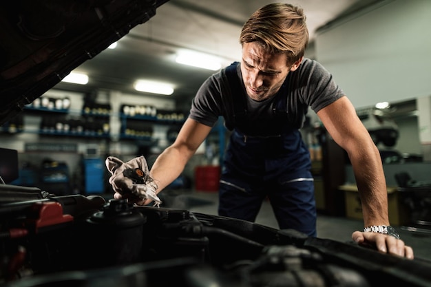 Photo gratuite mécanicien automobile ouvrant le bouchon du radiateur tout en maintenant le système de refroidissement de la voiture dans un atelier