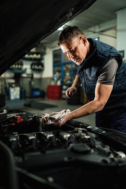 Mécanicien automobile vérifiant l'huile dans le moteur de la voiture tout en travaillant dans un atelier de réparation automobile
