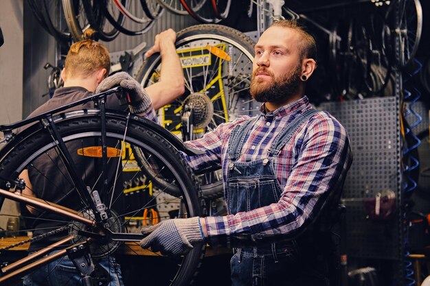 Mécanicien barbu à tête rouge fixant le dérailleur arrière d'un vélo dans un atelier.