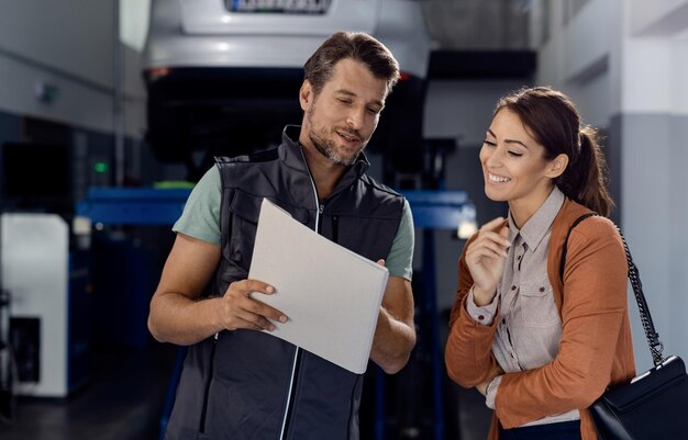 Mécanicien heureux et cliente passant par la paperasse à l'atelier de réparation automobile