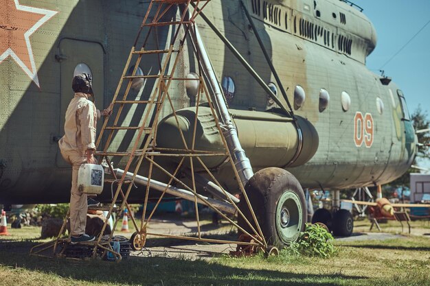 Un mécanicien en uniforme et casque volant effectue l'entretien d'un grand hélicoptère militaire dans le musée en plein air.