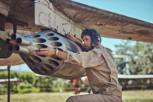 Un mécanicien en uniforme et un casque volant réparent un ancien chasseur-intercepteur de guerre dans un musée en plein air.