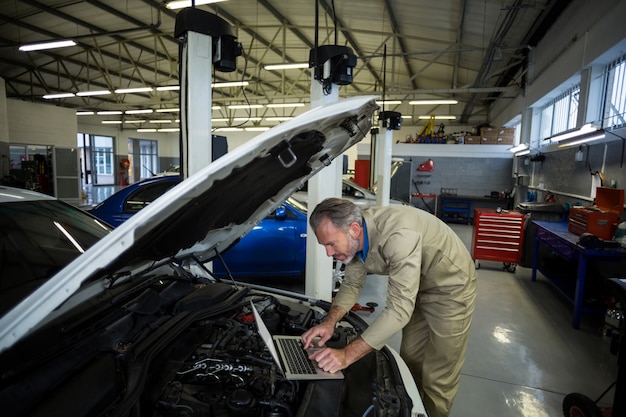 Mécanicien utilisant un ordinateur portable lors de l&#39;entretien d&#39;un moteur de voiture