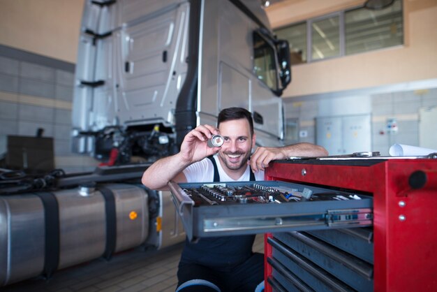 Mécanicien de véhicule debout par chariot d'outils tenant la pièce de rechange pour le service de camion