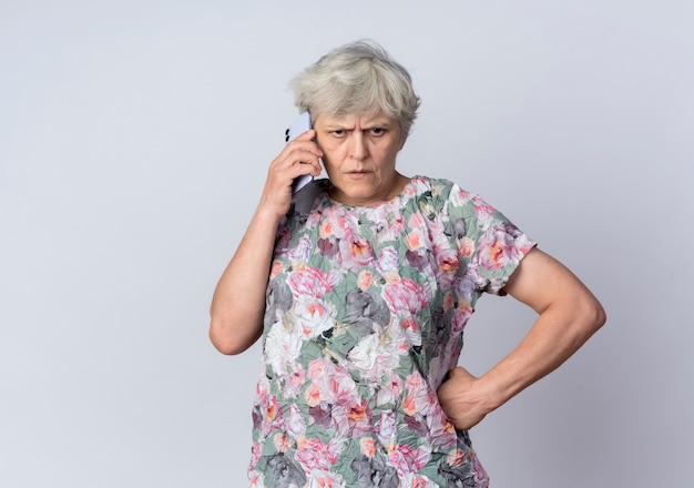 Mécontent femme âgée parle au téléphone isolé sur mur blanc