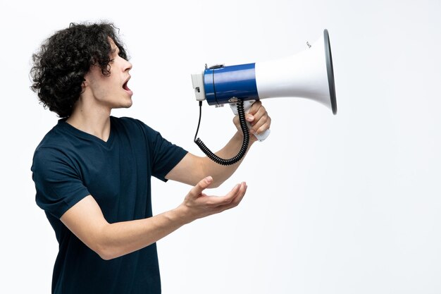 Mécontent jeune bel homme debout dans la vue de profil parlant dans le haut-parleur montrant la main vide regardant à côté isolé sur fond blanc