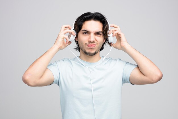 mécontent jeune bel homme regardant la caméra enlevant le casque isolé sur fond blanc