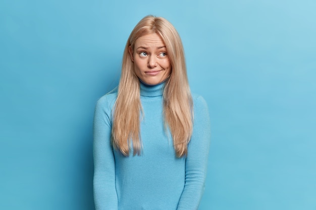 Mécontent jeune femme blonde aux cheveux longs semble bouleversé de côté a une expression réfléchie porte-monnaie lèvres porte col roulé