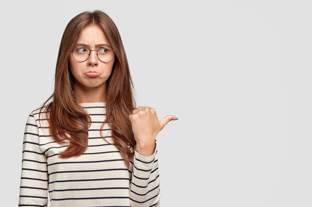 Mécontent jeune femme avec des lunettes posant contre le mur blanc