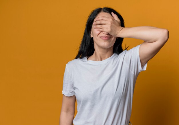 Mécontent jeune fille caucasienne brune ferme les yeux avec la main isolée sur le mur orange