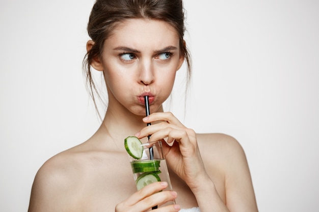 Mécontent jeune fille de l'eau potable avec des tranches de concombre sur fond blanc. Cosmétologie de beauté et spa. Traitement facial.