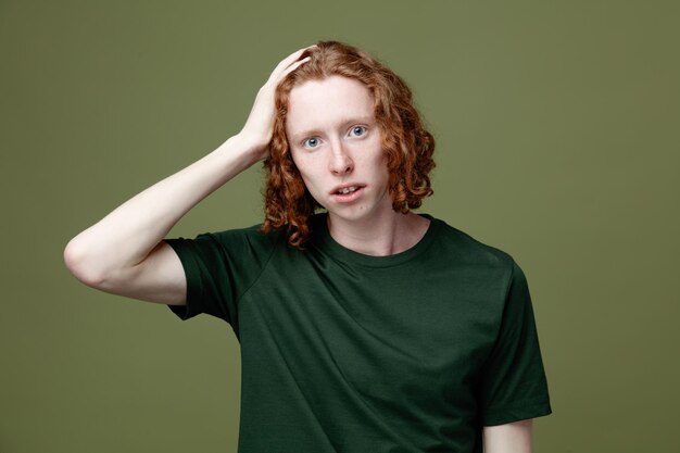 Mécontent de mettre la main sur la tête jeune beau mec portant un t-shirt vert isolé sur fond vert